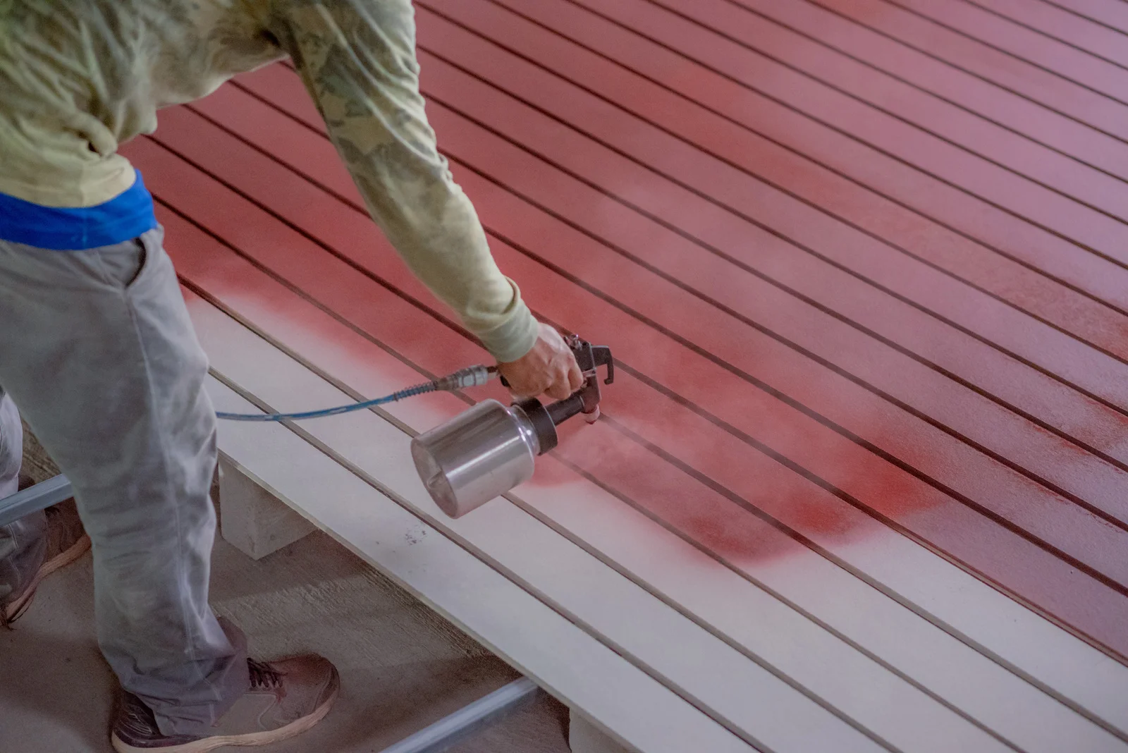 Worker red spray painting wooden decking
